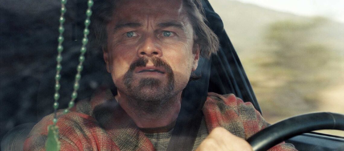Leonardo DiCaprio looking concerned in the driver's seat of a car from One Battle After Another backtothepicture.net still