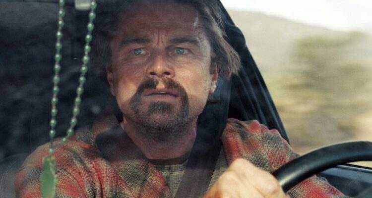 Leonardo DiCaprio looking concerned in the driver's seat of a car from One Battle After Another backtothepicture.net still